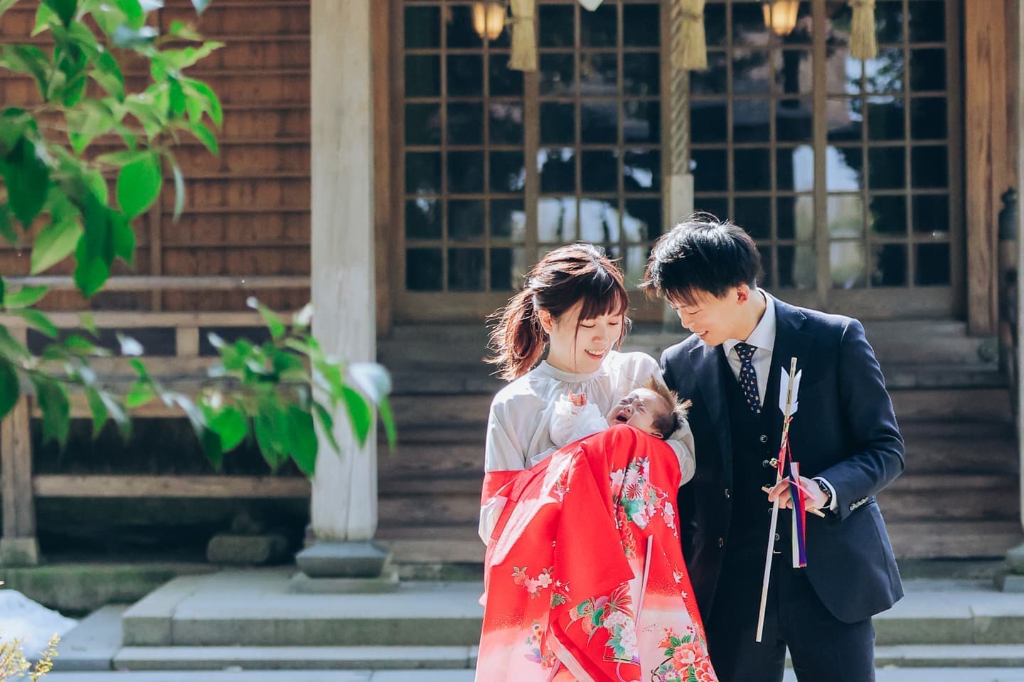 神社の前で赤いお宮参りの晴れ着を着た女の子と両親