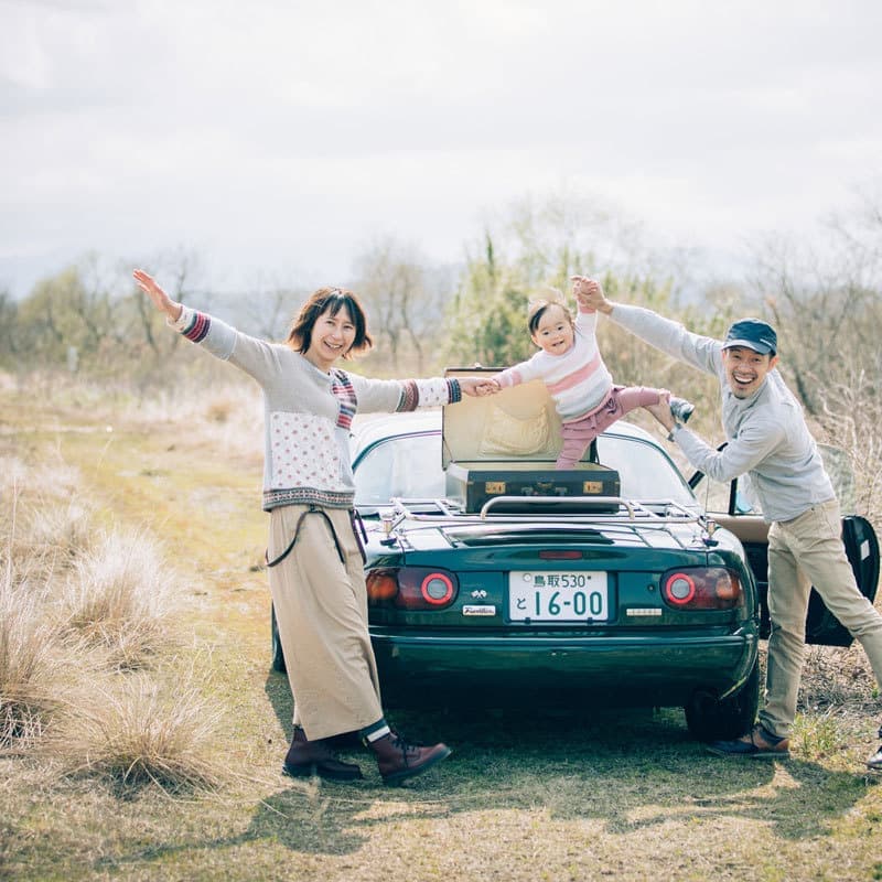 マツダロードスターとベージュのパンツ白いシャツでコーディネートした家族の